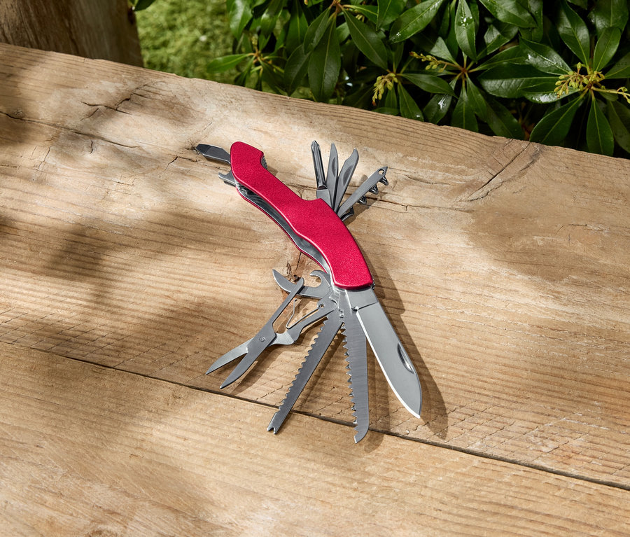 Un outil multifonction rouge est ouvert sur une surface en bois.