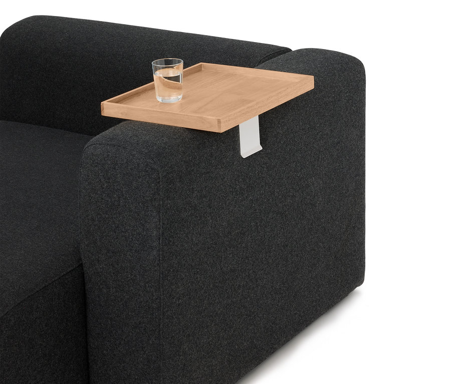 Sur l'accoudoir d'un canapé gris se trouve un plateau en bois avec un verre d'eau.