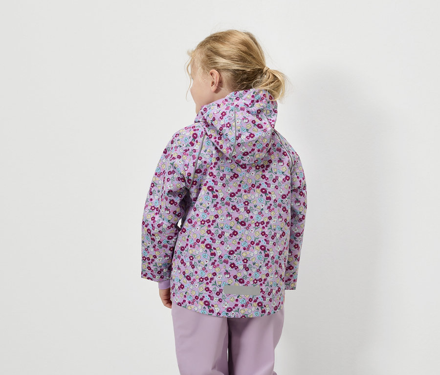 Vue de dos, une petite fille aux cheveux blonds porte une veste lilas à motif floral et un pantalon assorti.