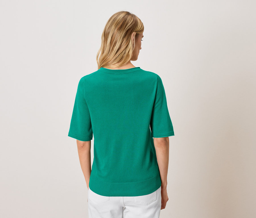 Vue de dos d'une femme blonde portant un haut à manches courtes vert émeraude et un pantalon blanc.