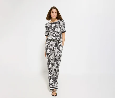 Une femme aux cheveux bruns porte un haut à manches courtes noir et blanc et un pantalon à imprimé floral.
