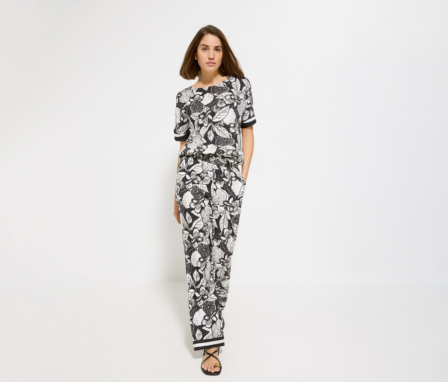 Femme portant un haut à fleurs et un pantalon large Olsen. Elle porte des sandales noires.