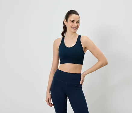 Une femme portant un soutien-gorge de sport et un legging bleu marine pose devant un fond blanc.