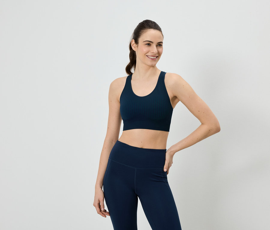 Une femme portant un soutien-gorge de sport et un legging bleu marine pose devant un fond blanc.