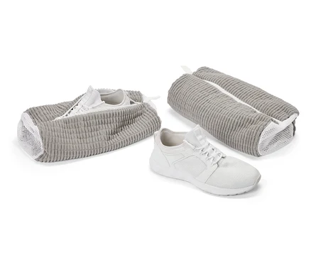 Une basket blanche devant un sac à chaussures gris. Une autre chaussure dans un sac ouvert, un troisième sac est fermé.