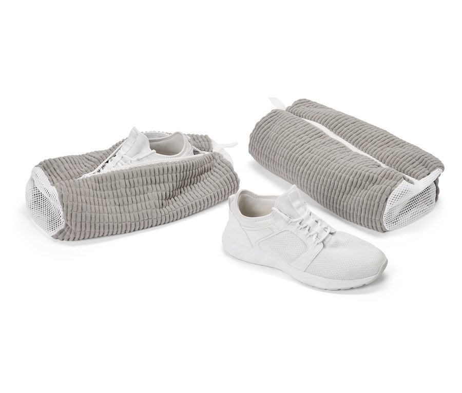 Une basket blanche devant un sac à chaussures gris. Une autre chaussure dans un sac ouvert, un troisième sac est fermé.
