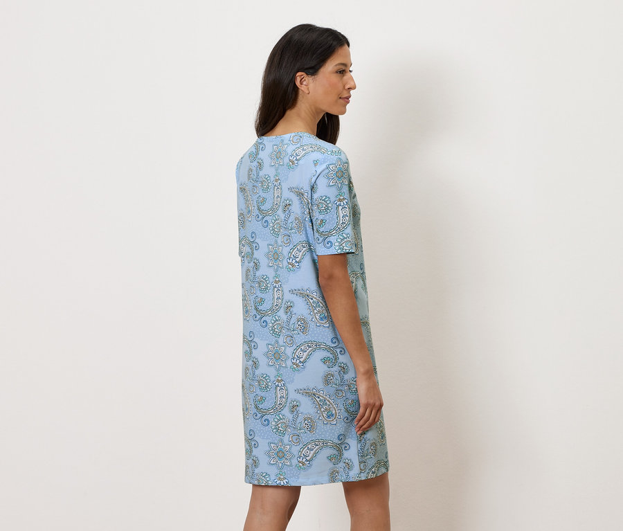 Femme debout de profil portant une robe bleu clair à fleurs.