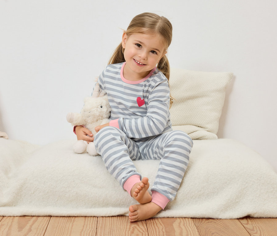 Une petite fille blonde est assise sur un coussin et tient un mouton en peluche.