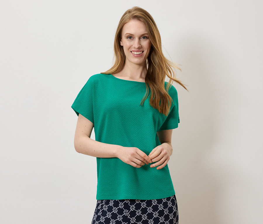 Femme souriante portant un haut vert et une jupe avec un motif blanc et bleu marine.