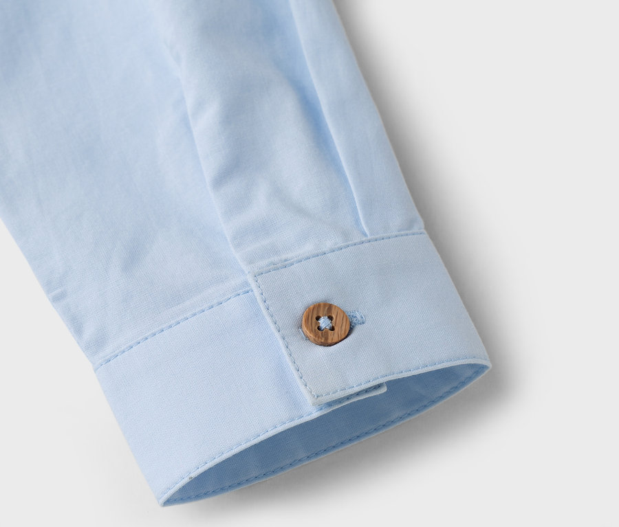 Gros plan sur la manche d'une chemise bleu clair avec un bouton marron.