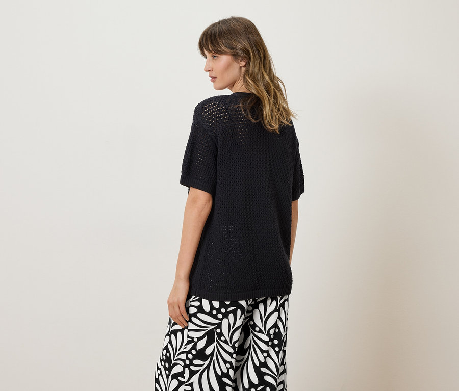 Femme vue de dos portant un haut en tricot noir et un pantalon à motifs.
