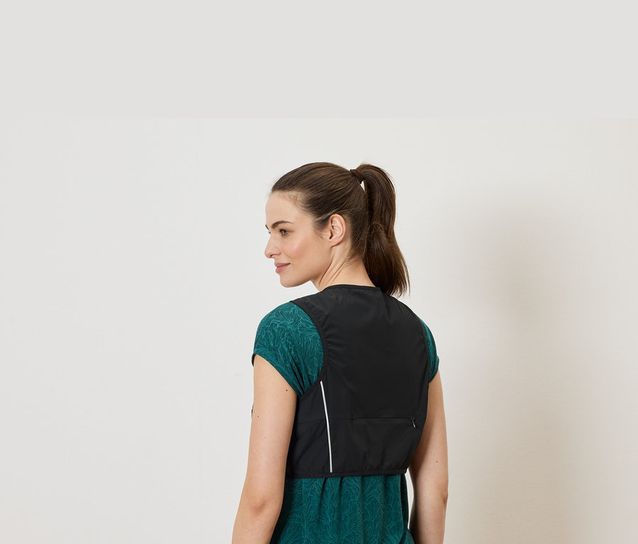 Une femme portant une queue de cheval porte un gilet noir sur un haut vert.