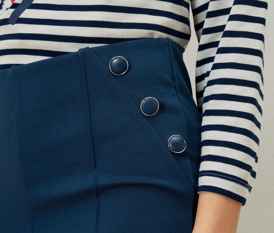 Gros plan d'une femme portant une jupe bleue boutonnée et un haut rayé.