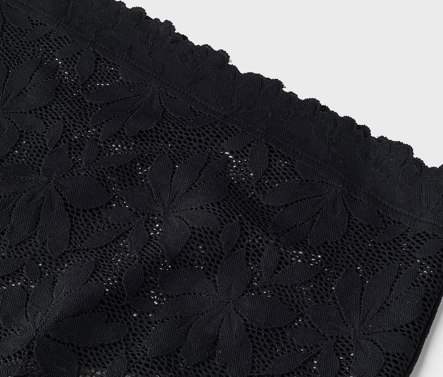 Gros plan sur de la dentelle noire avec un motif floral et un bord ondulé.