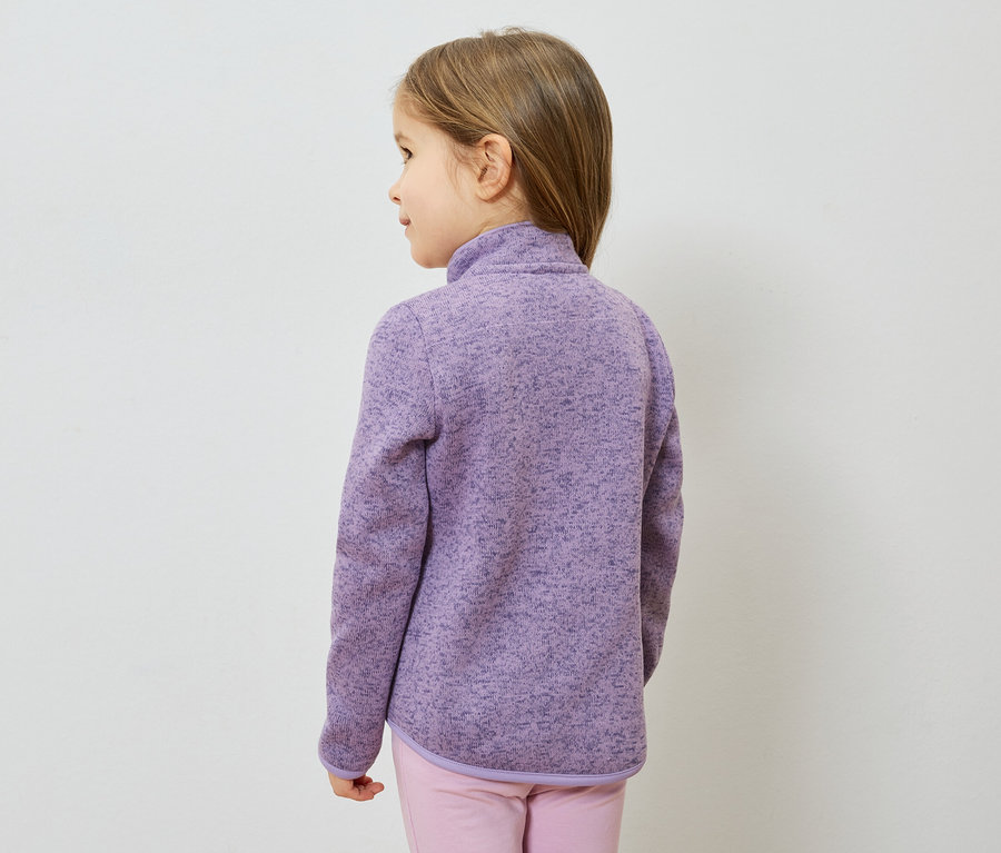 Fillette vue de dos, portant une veste en polaire violette et un pantalon rose sur fond blanc.
