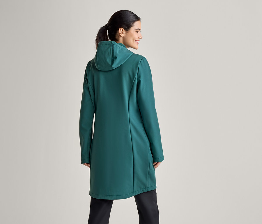 Une femme avec une queue de cheval, vue de dos, porte un manteau vert à capuche et un pantalon noir.