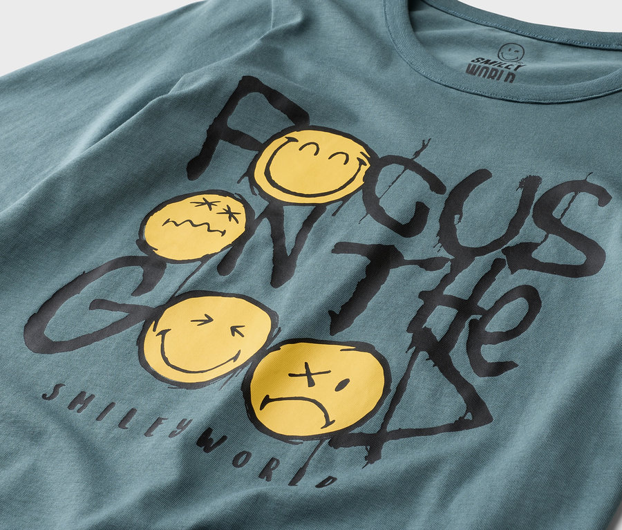 Gros plan sur un t-shirt à manches longues bleu pétrole Smiley World avec l'inscription « Focus on the Good » et des smileys jaunes.