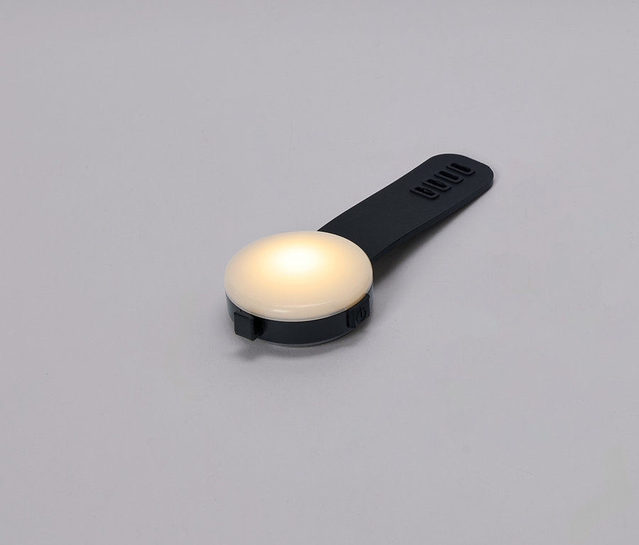 Gros plan d'une petite lampe ronde et lumineuse avec une poignée noire sur un fond gris.