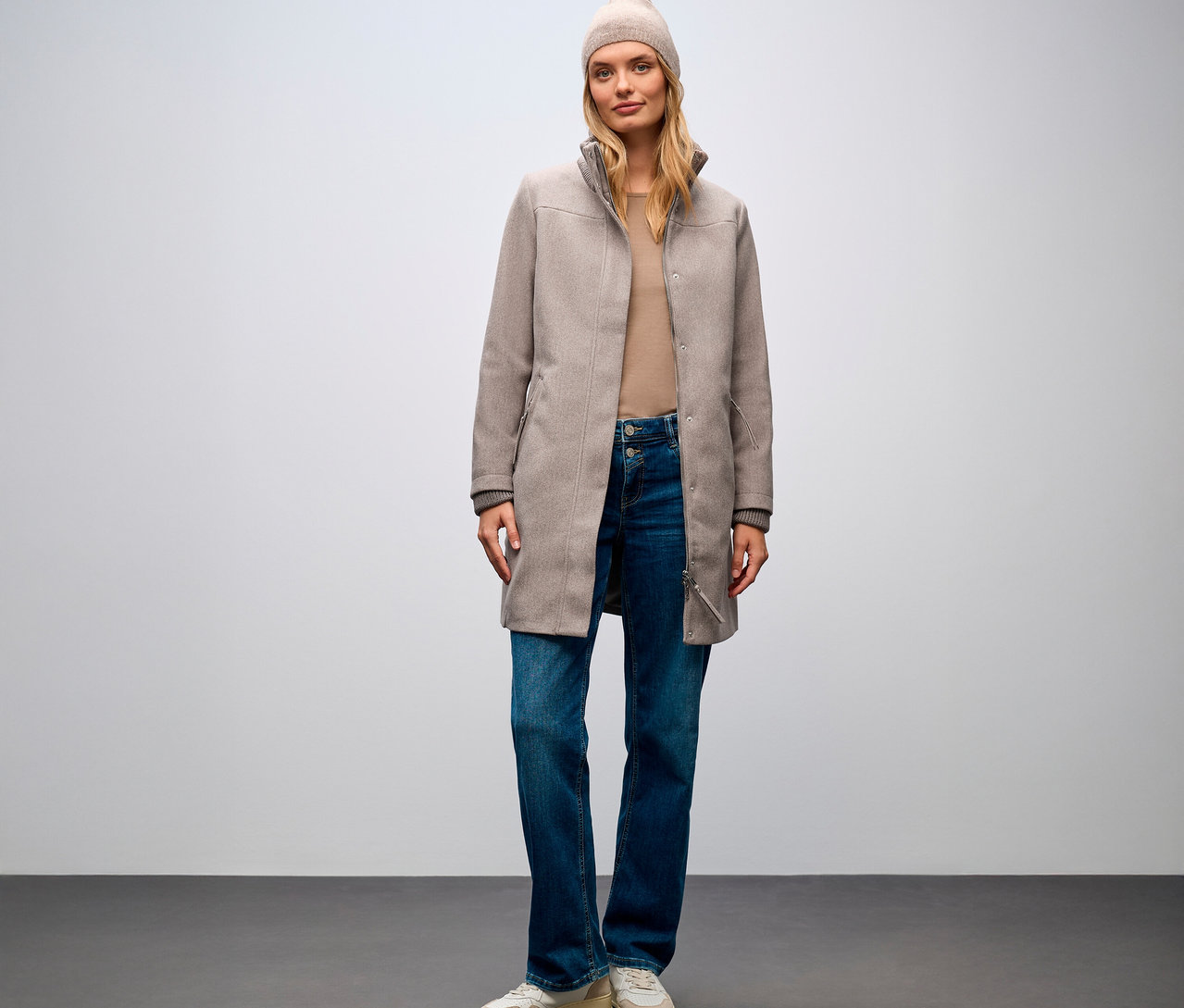 Femme debout portant un manteau court Street One, un jean et un bonnet.