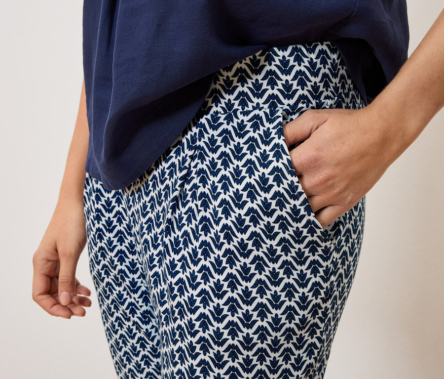 Gros plan d'une personne portant un pantalon bleu marine à motifs blancs et un haut bleu marine, avec une main dans la poche du pantalon.