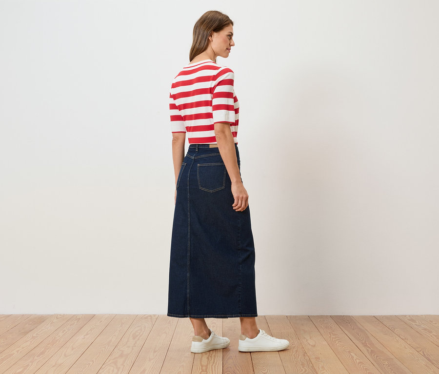 Femme vue de dos portant un haut rayé rouge et blanc, une jupe longue en jean et des baskets blanches.