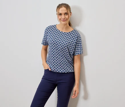 Femme portant un t-shirt à motifs bleu et blanc et un pantalon bleu, une main dans la poche.