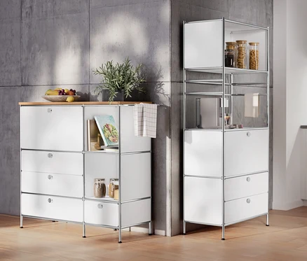 Dans la pièce, un meuble en métal « CN3 » avec plateau en bois, 1 abattant et 4 tiroirs, blanc et une étagère en métal « CN3 » avec 1 abattant et 2 tiroirs.