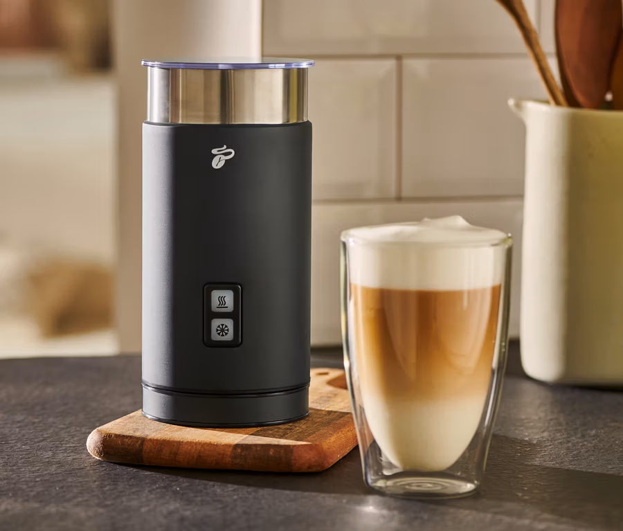 Un mousseur à lait électrique noir est placé à côté d'un verre de café au lait.