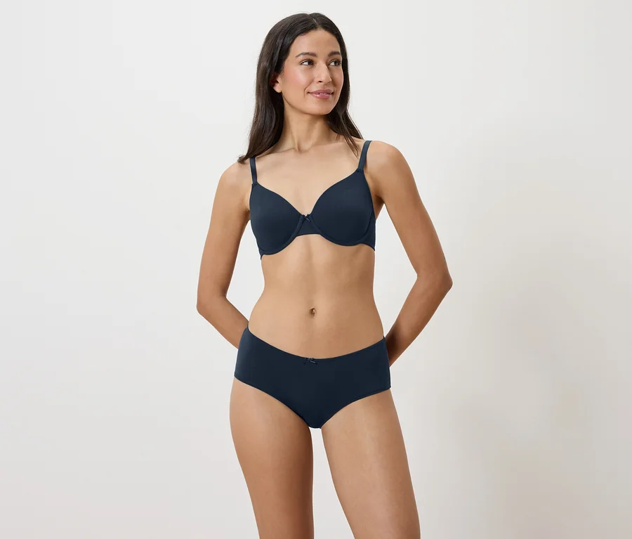 Une femme pose sur un fond blanc en soutien-gorge et culotte bleu marine.