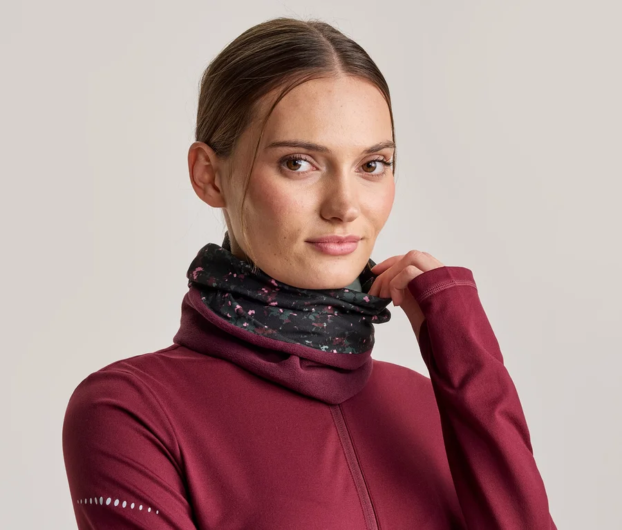Femme portant un haut à manches longues bordeaux et un cache-cou noir à motifs floraux, ajustant le cache-cou avec sa main.