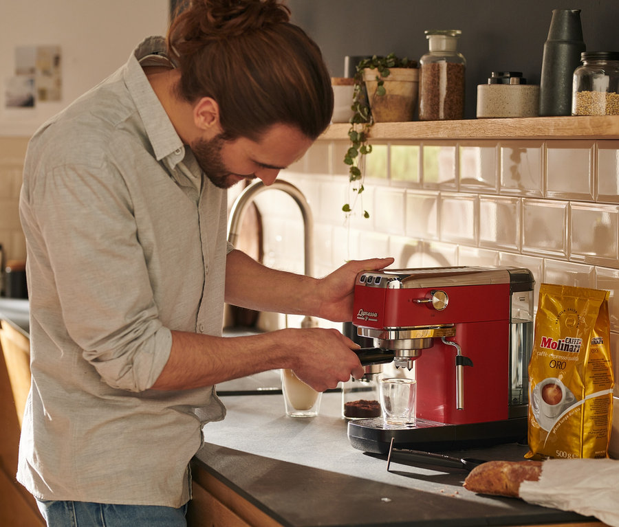 Un homme prépare du café avec une machine à porte-filtre « Lapressa » rouge.