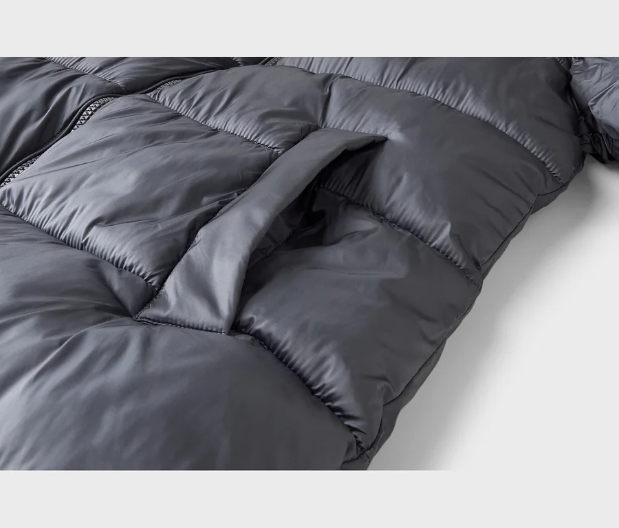 Gros plan d'une doudoune matelassée gris foncé et brillante avec une poche latérale visible et une fermeture éclair.