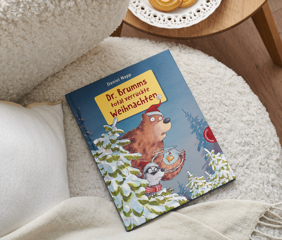 Le livre « Dr. Brumms total verrückte Weihnachten » est posé sur un fauteuil à côté d'un coussin.