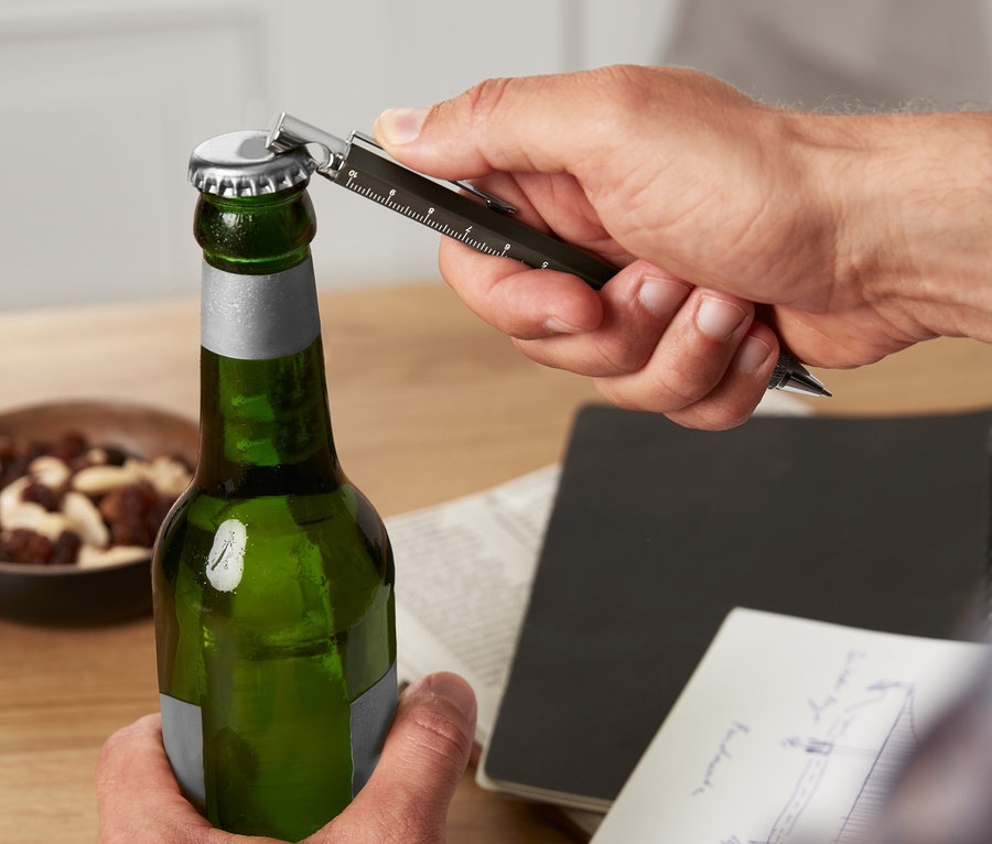 Un homme ouvre une bouteille verte avec un stylo multifonction.