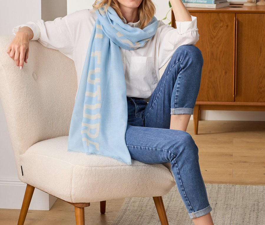 Femme assise sur un fauteuil portant une écharpe tissée avec inscription imprimée.