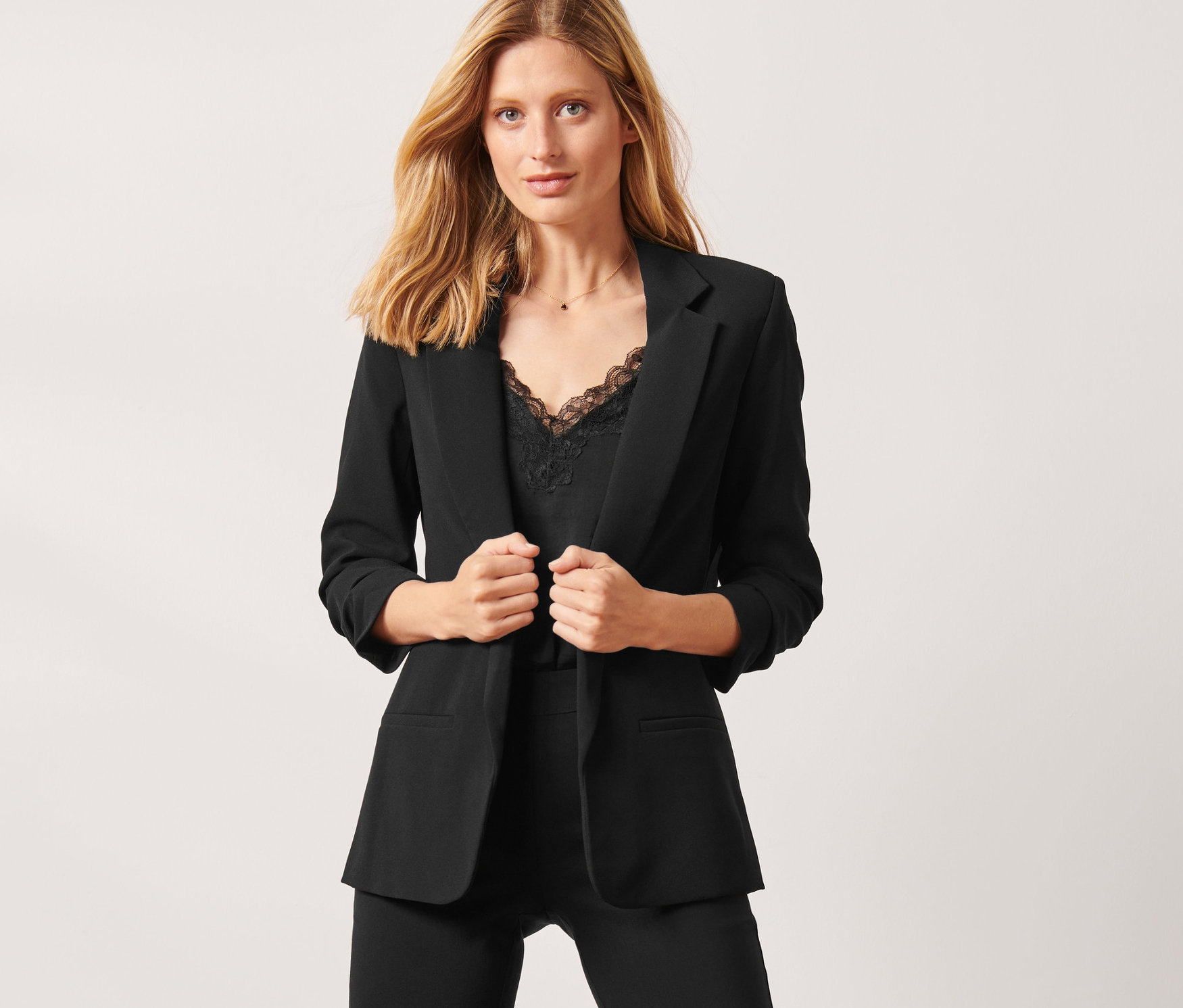 Une femme porte un blazer noir à manches froncées, un pantalon noir et un haut.