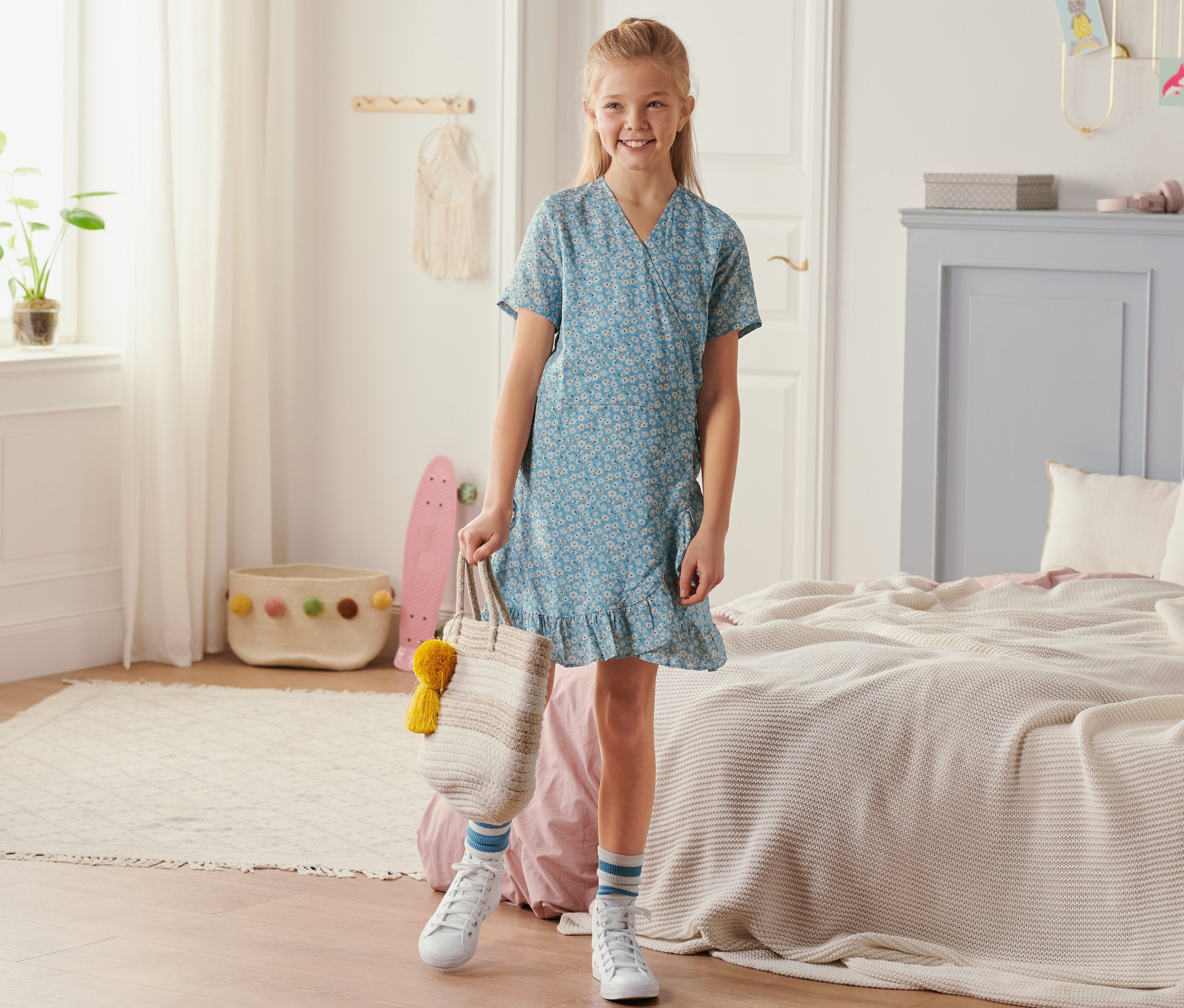 Une fillette souriante se tient dans une pièce et porte une robe portefeuille.