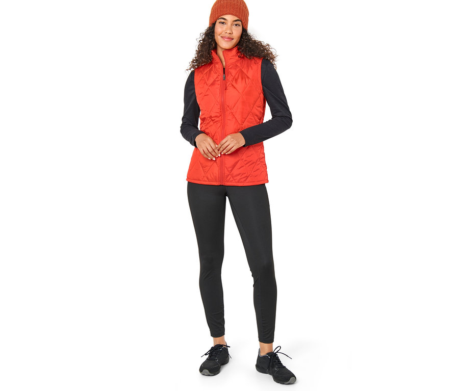 Une femme portant un manteau de pluie 3-en-1 orange avec un gilet et un bonnet marron.