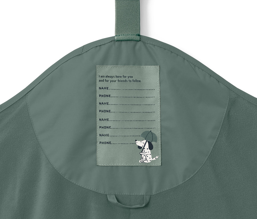 Gros plan sur un pantalon de pluie thermique pour enfant, vert foncé, avec une étiquette pour le nom et le numéro de téléphone.