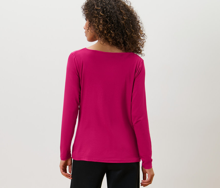 Vue arrière d'une femme aux cheveux bruns et bouclés portant une blouse avec encolure en cascade et un pantalon noir.