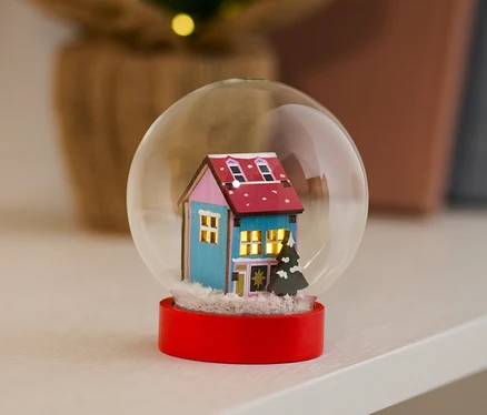 Boule à neige à LED avec une maison bleue et une base rouge posée sur une étagère.
