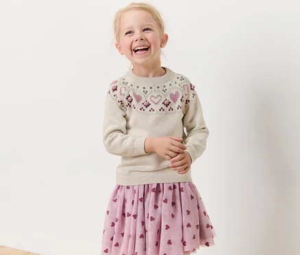 Fillette blonde souriante portant un pull en maille pour enfant.