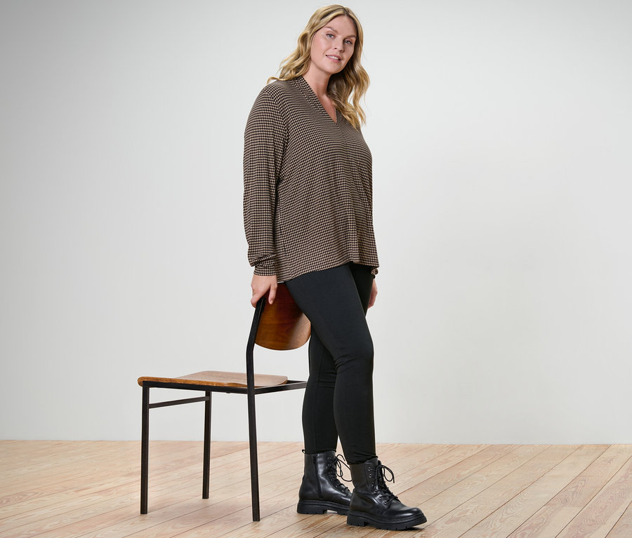 Femme posant en blouse imprimée avec encolure en V et legging heavy à côté d'une chaise.