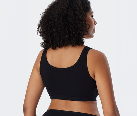 Femme vue de dos, légèrement tournée vers la droite, portant une brassière SCHIESSER noire et des sous-vêtements noirs.