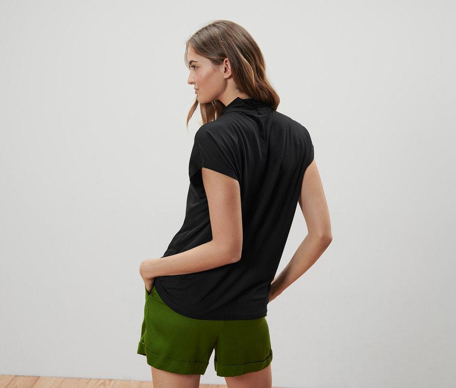 Une femme pose dos à la caméra et porte un chemisier noir à encolure en V et un short vert.