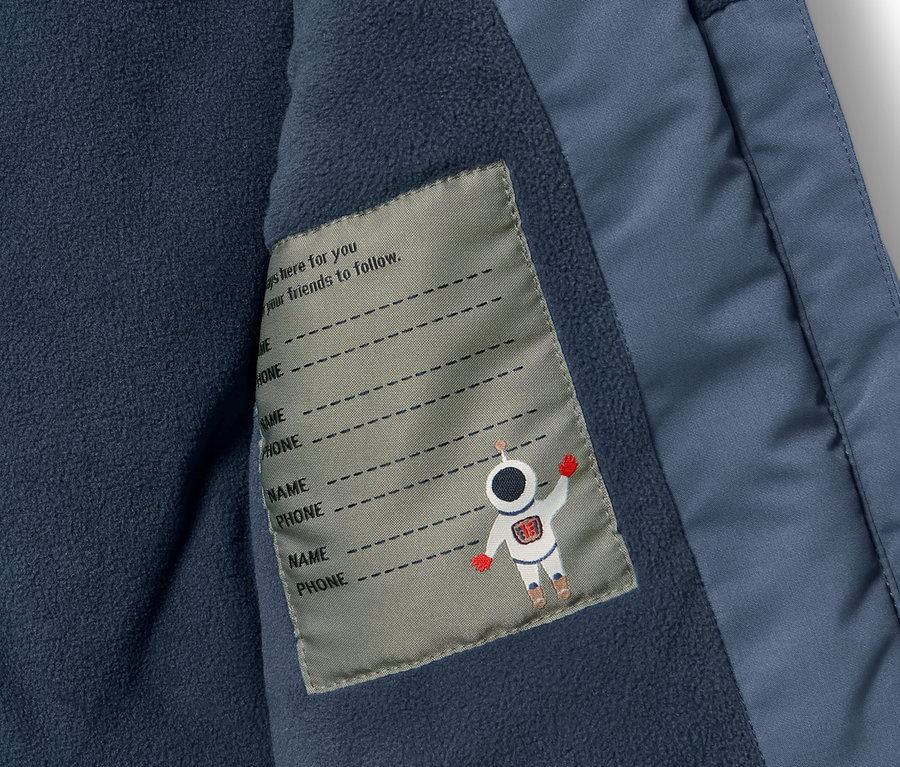 Détail d'une combinaison de ski pour enfant avec poche intérieure et étiquette pour le nom.