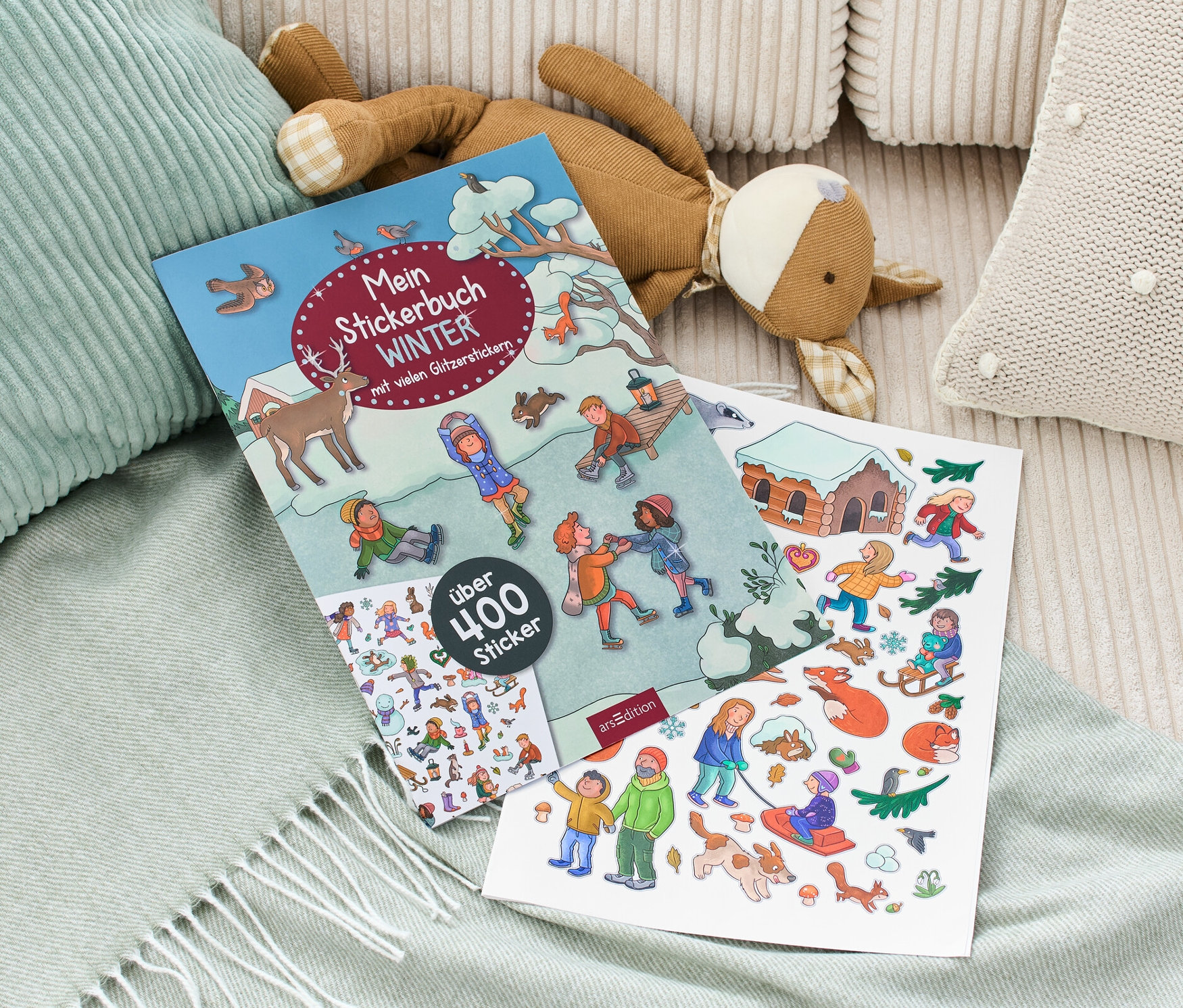 Sur une couverture se trouvent le « Mein Stickerbuch Winter » et une peluche.
