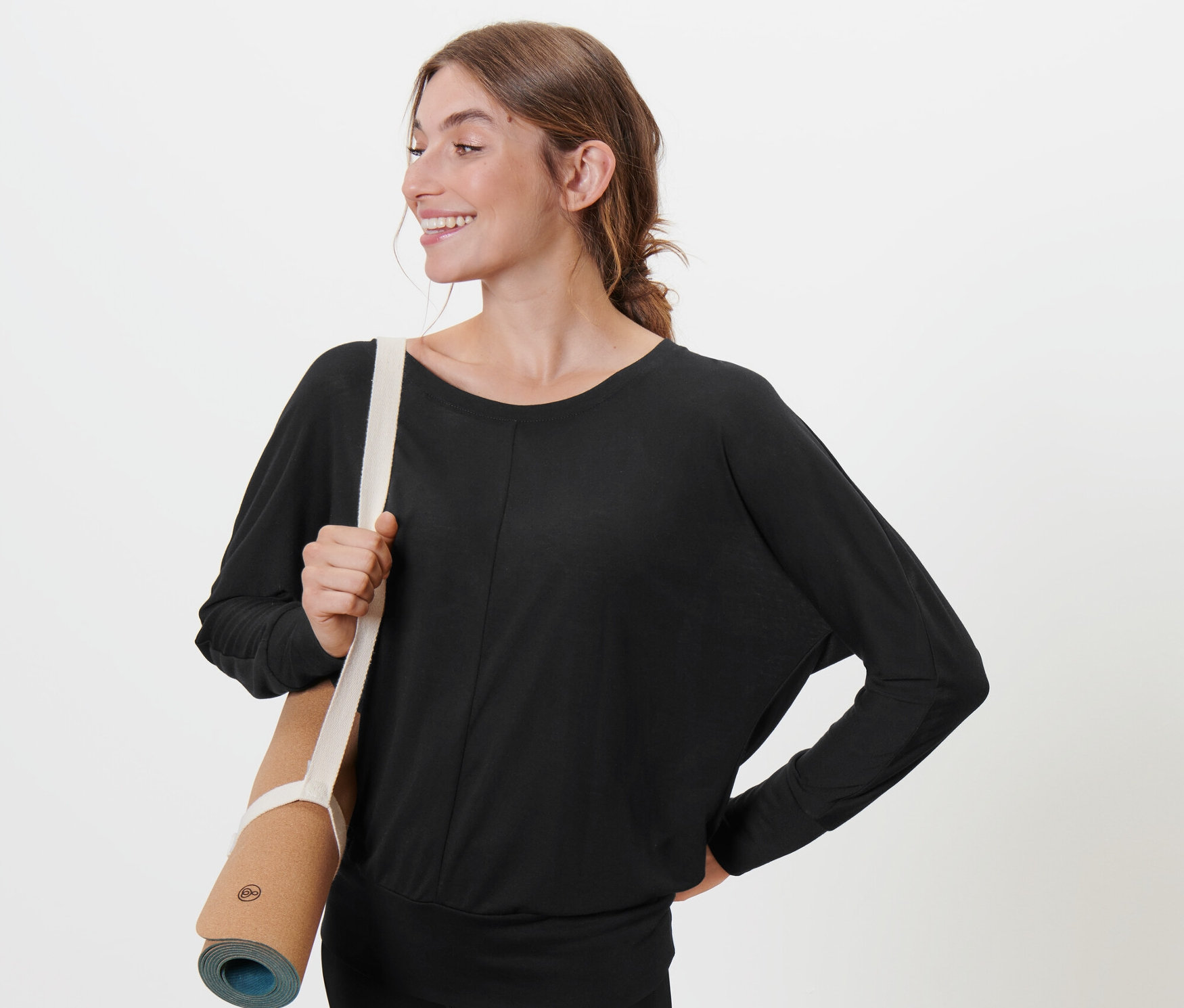 Femme portant un tapis de yoga sur l'épaule, portant un t-shirt de sport et de yoga noir.