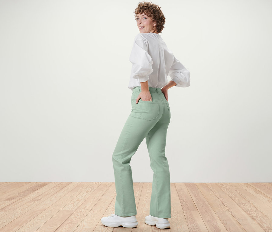 Femme regardant par-dessus son épaule et posant en jean bootcut vert menthe Coupe « Lou » et chemisier blanc.
