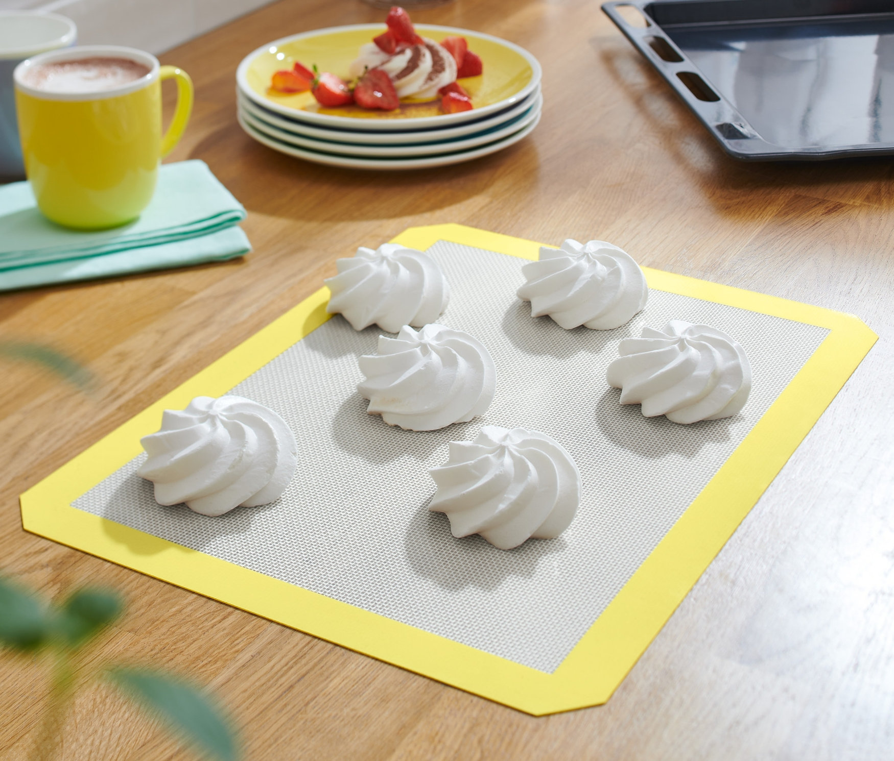 Sur une table en bois, un tapis de cuisson renforcé en fibres de verre jaune avec six meringues blanches.